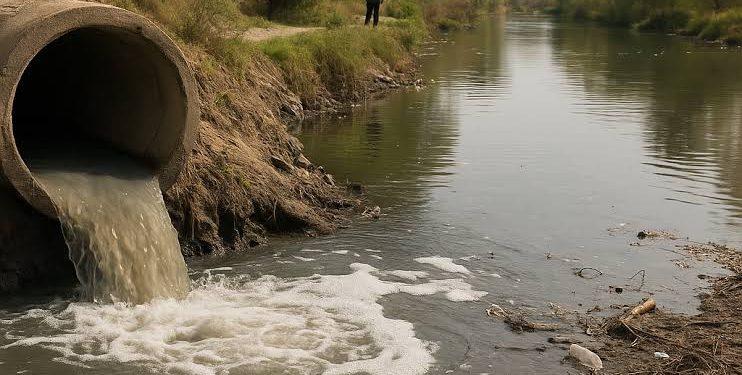 Concrete pipe discharging murky water into a canal; a person stands in the background on the bank.