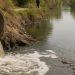 Concrete pipe discharging murky water into a canal; a person stands in the background on the bank.