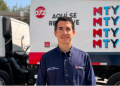 Man in a navy uniform standing in front of a branded delivery truck with MTY graphics in red and blue.